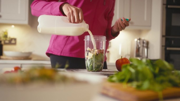 厨房里穿着健身服的妇女将新鲜的食材混合到健康的冰沙饮料中