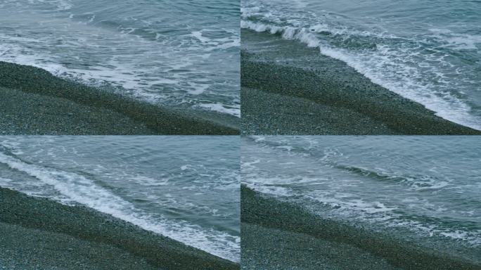 海岸上的平静海浪。海浪和冲浪是在海滩上溅起沙子和小鹅卵石。不动。