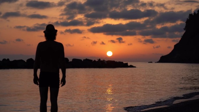 单身男人的剪影，独自欣赏海边火红的夕阳和天空的红色——渴望假期和天空中的加勒比色彩——体验大自然的美