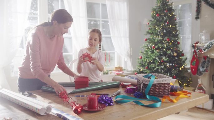 母亲和女儿在家里包装圣诞礼物的慢动作肖像。可爱的小女孩为送给家人的礼品盒挑选装饰品。充满爱和分享的节