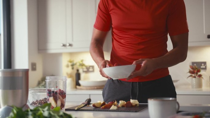 在家厨房里穿着健身服的男人将水果和菠菜混合成健康饮料