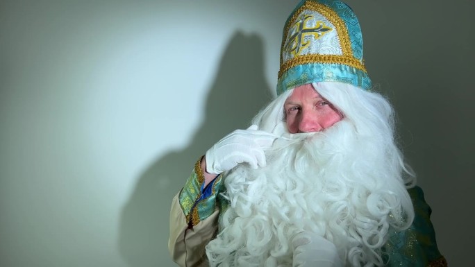圣尼古拉斯目不转睛地盯着他的胡子，他的胡子疑惑地看着镜头上白色背景上的影子，神奇的工人尼古拉斯，圣诞