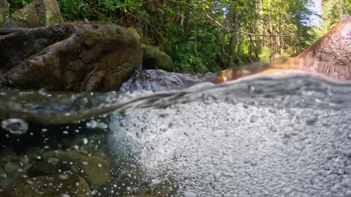 高山河流中最纯净的气泡水。半水下慢动作拍摄的河流在绿色的森林和山脉。石头之间有小瀑布的小溪