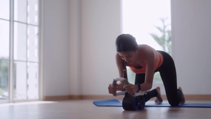 一位穿着运动服的亚洲女性正在家里的瑜伽垫上使用健身车来增强腹部肌肉，以保持健康