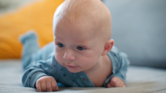 宝宝的俯卧时间。一个蓝眼睛的小男孩趴在肚子上的特写
