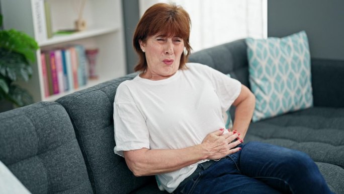 中年妇女因胃痛坐在家里的沙发上