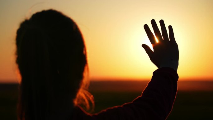 日落时小孩的手特写。阳光穿过手指。太阳下一只手的剪影。夕阳下快乐女孩的剪影。信仰上帝是一种宗教观念。