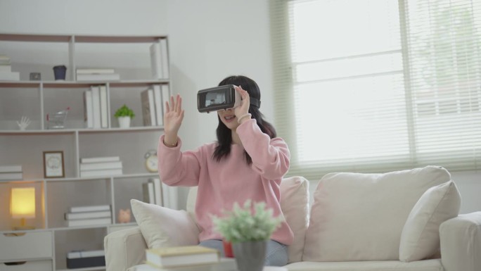 亚洲女人微笑着玩VR游戏，3D眼镜在家里客厅娱乐，亚洲女人在家里度假快乐。快乐女人玩虚拟现实技术概念