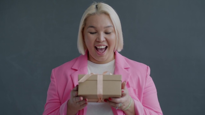 快乐的亚洲女士拿着漂亮的礼盒，看着镜头表达喜悦的慢动作肖像