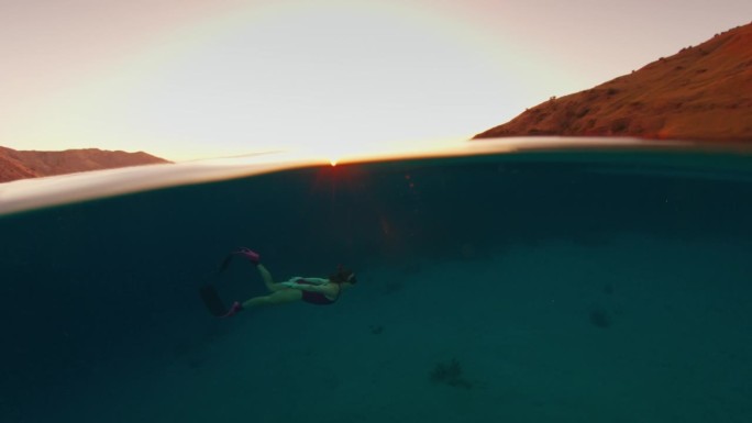 日落时分在热带海洋中游泳的女子的电影胶片。冻结的海面框架和移动的水下模型