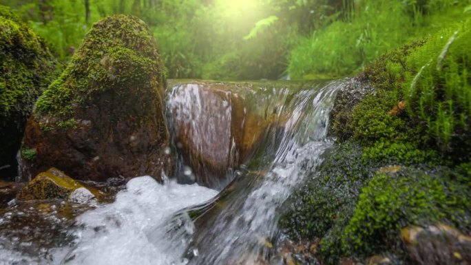 河水清澈，在长满青苔的石头间流动。云台慢动作拍摄的山涧与小瀑布被绿草包围