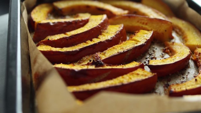 美味的烤南瓜片，加入橄榄油，香草和盐，新鲜出炉，放在烤盘上的纸上。关闭了。