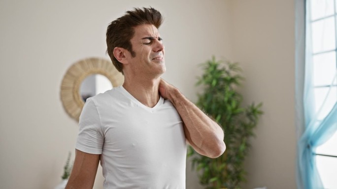 年轻的西班牙裔男子忍受着颈椎疼痛站在家里