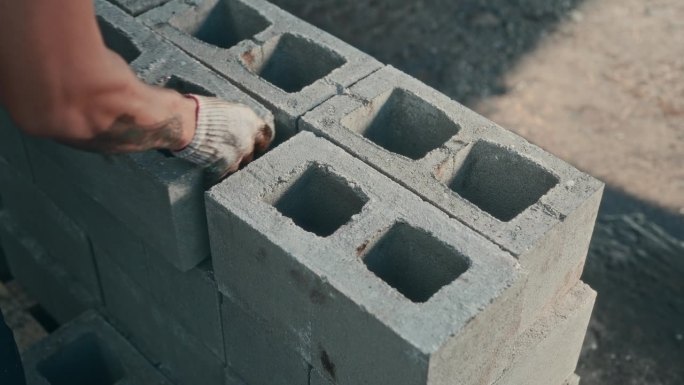 一个无法辨认的男性杂工在建筑工地铺设煤渣砖。艰苦的非技术劳动