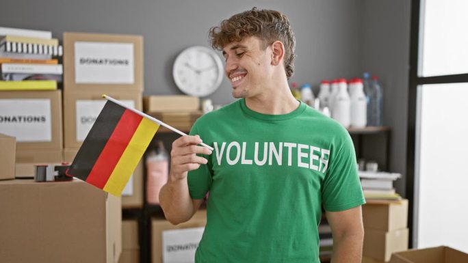 暖心的肖像，微笑的年轻西班牙人，一个慈善中心的志愿者，自豪地举着德国国旗