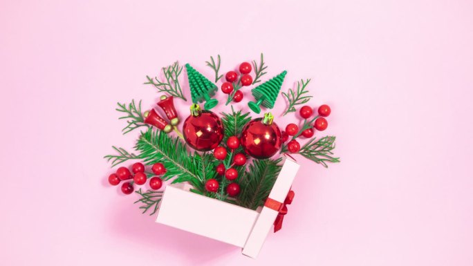 圣诞装饰品和小圣诞树旁边的粉色礼品盒。树杈出现又消失。粉红色的背景。
