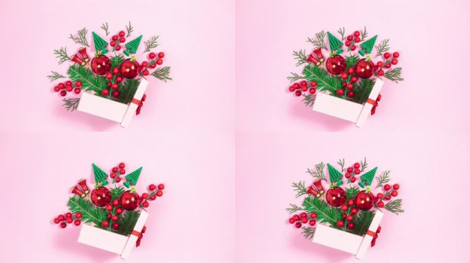 圣诞装饰品和小圣诞树旁边的粉色礼品盒。树杈出现又消失。粉红色的背景。