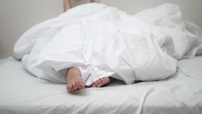 躺在床上的女人，光着脚从毯子里伸出来，愉快地伸伸身子醒来，迎接新的一天。