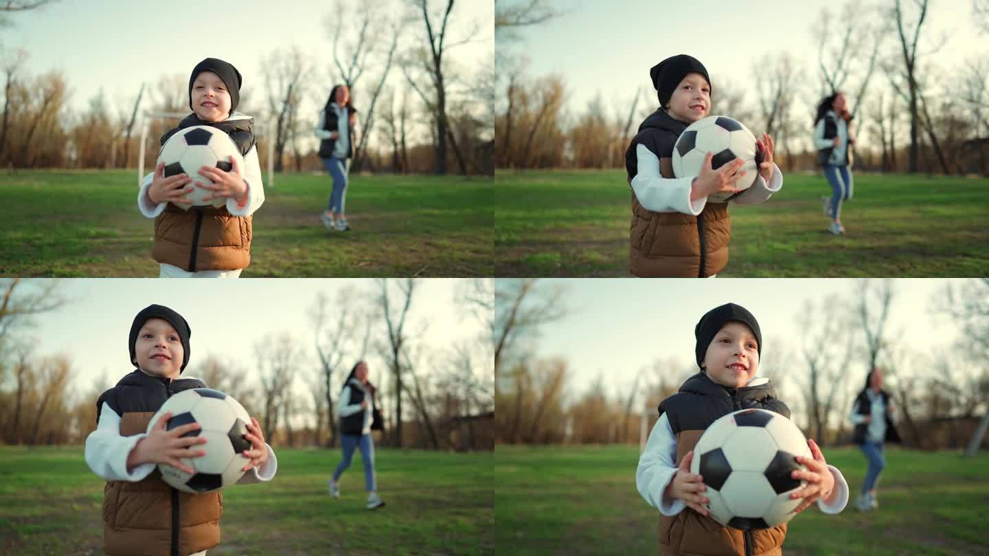 快乐的男孩手里拿着黑白相间的足球在公园里奔跑。缓慢的运动。小孩在公园里玩。