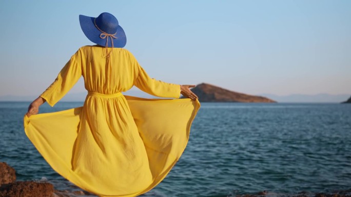 身穿黄色连衣裙的女人对着大海。