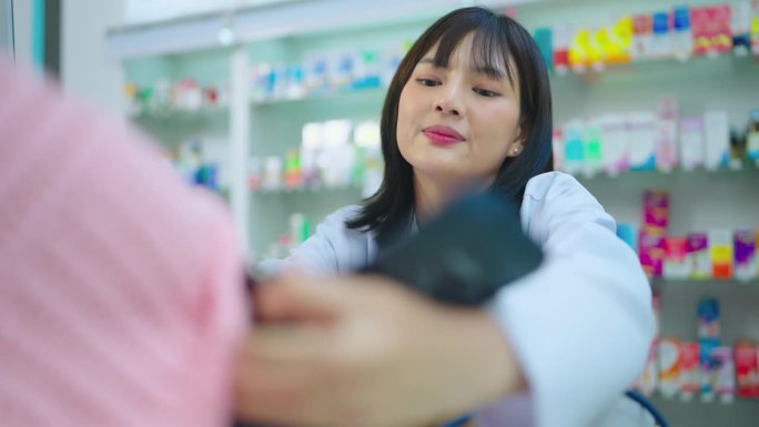 亚洲美丽的女药剂师测量血压与高级妇女在药店。