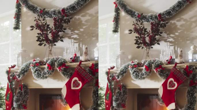 垂直屏幕:空镜头描绘一个和平的下雪的圣诞节早晨。近距离观察圣诞树旁装饰着长袜的壁炉。绿色和红色的花环