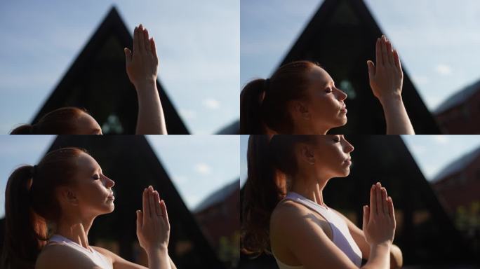 在夏天阳光明媚的早晨，精神上的年轻女子站在阳光的背景下，与自然和谐地冥想着合十手印。