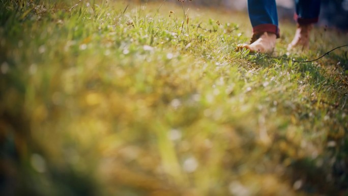 近距离的赤脚女人走在阳光明媚的草地上