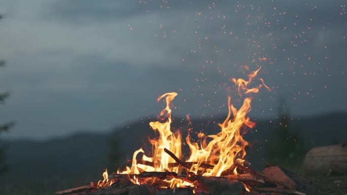 游客燃起篝火，火花在空中飞舞，慢动作拍摄。黄昏的篝火映衬着群山和森林