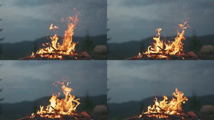 游客燃起篝火，火花在空中飞舞，慢动作拍摄。黄昏的篝火映衬着群山和森林