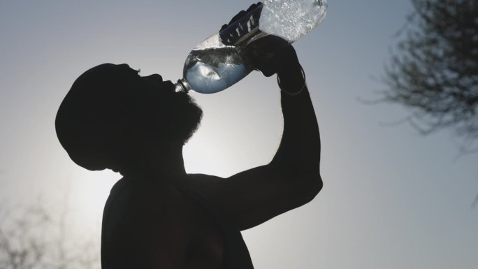 一个非洲黑人男子侧影从瓶子里喝水。气候变化，全球变暖，高温