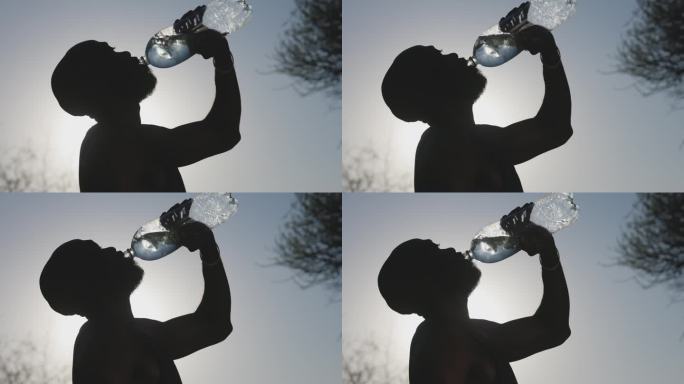 一个非洲黑人男子侧影从瓶子里喝水。气候变化，全球变暖，高温
