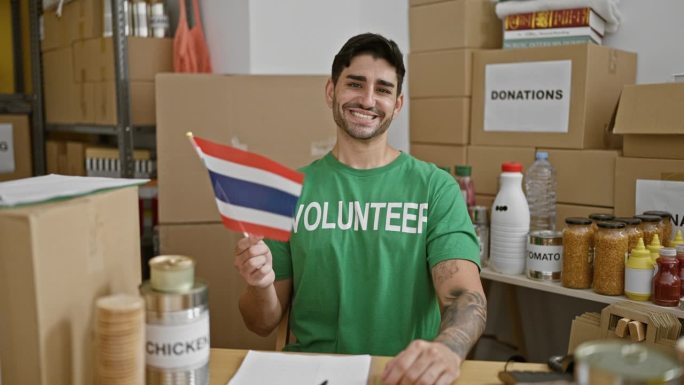 在慈善中心，年轻的西班牙裔志愿者面带微笑，自信地举着泰国国旗