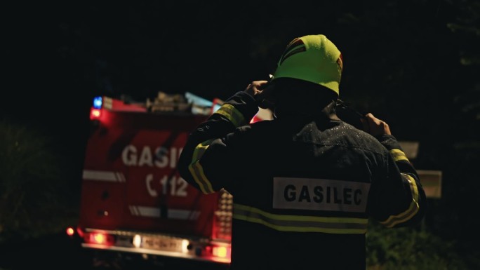 夜间道路上，无名消防员在消防车前戴上头盔