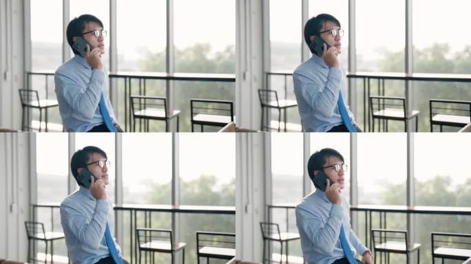 一名年轻的亚洲男性职员正坐在办公室的吧台桌旁，用智能手机预约和朋友一起喝酒。