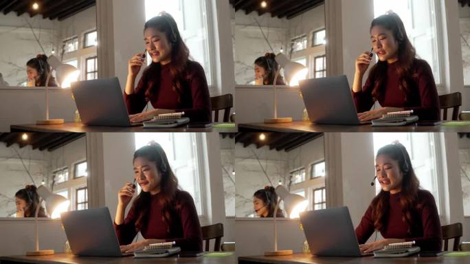 年轻开朗的女子坐在家里办公室的办公桌前，戴着耳机上网聊天。愉快的女接线员看着屏幕。远程工作概念。