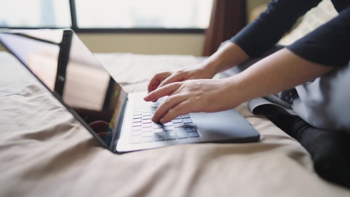 男子躺在床上用笔记本电脑键盘打字的特写镜头