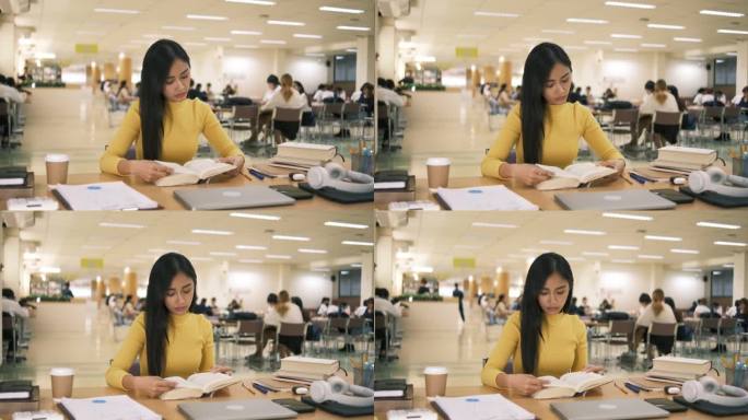 亚洲学生女孩坐在桌边一边看书一边做作业，用笔记本电脑在国外通过网友联系打视频电话，在图书馆里开心地笑