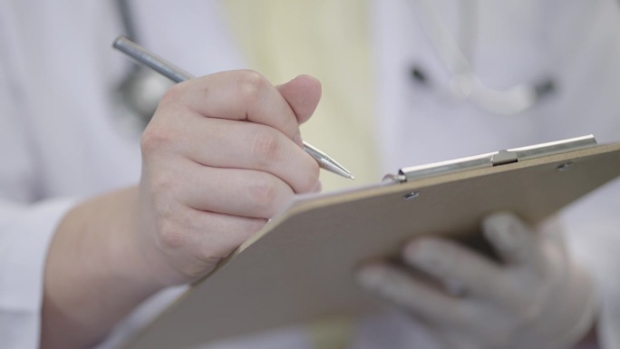 图为医生在医院体检结束后，在检查室用钢笔在记事本上书写病历的特写。
