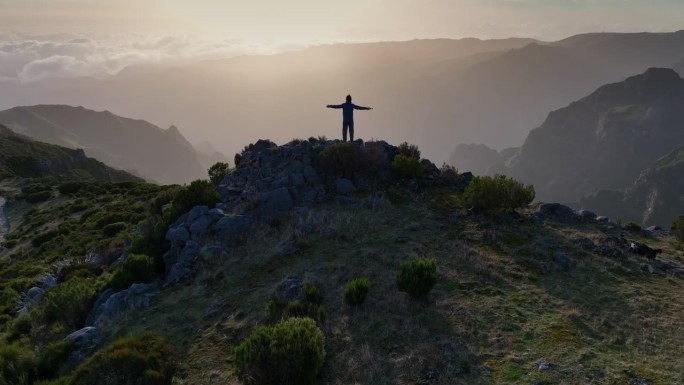 一个人站在山顶上看日落。攀登者在山顶。无人机拍摄。胜利、成功、成就、自由的概念