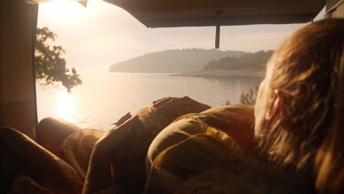 在阳光明媚的日子里，放松的孕妇在面包车上享受美丽的湖泊，同时抚摸着她的肚子