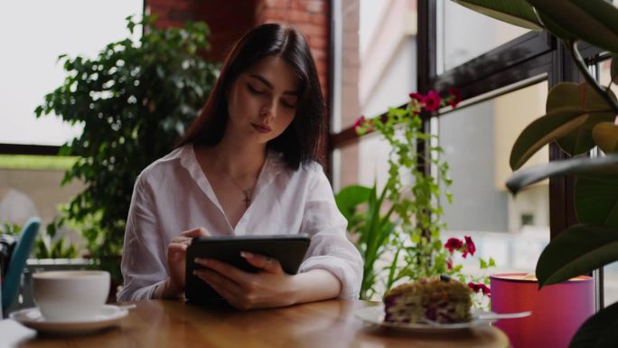 在咖啡馆用平板电脑上网的年轻成年女性，忙碌的女商人的肖像