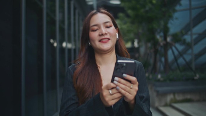 年轻的亚洲女商人在城市街道上行走时使用手机