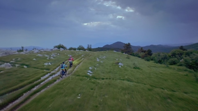 两名山地自行车手在暴风雨前的日落后从山上骑下来