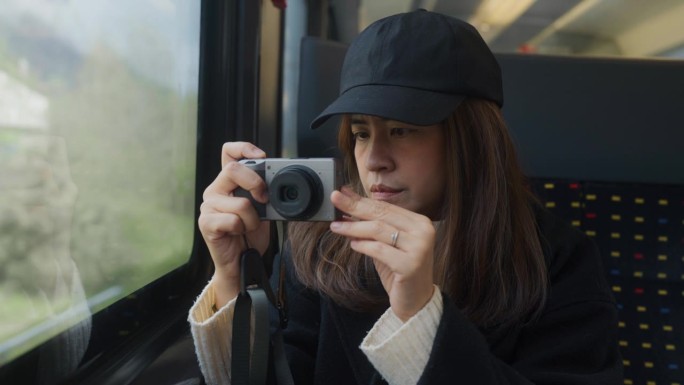 亚洲女游客在瑞士乘火车旅行时，从车窗拿起相机拍照。