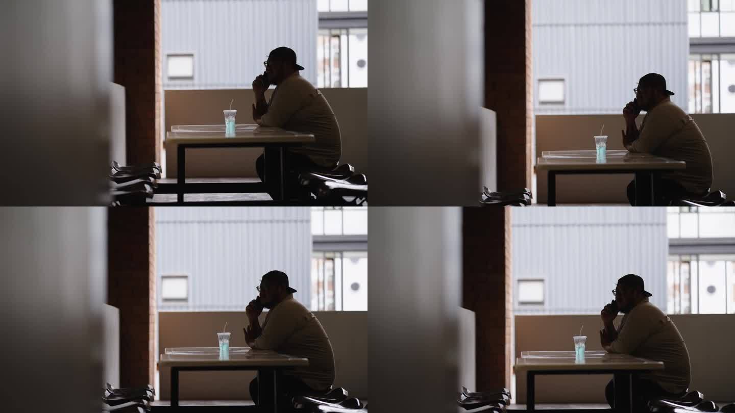 一名体重超标的男学生在短暂的休息时间，坐在大学阳台的长椅上，桌上放着一杯冰苏打水，一边用手机和朋友聊