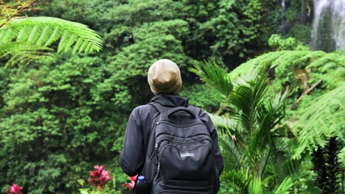 成年男子在绿色自然中前往森林瀑布。年轻的不认识的人走到瀑布的旅行目的地。海岛天堂景观中个人旅行的生活