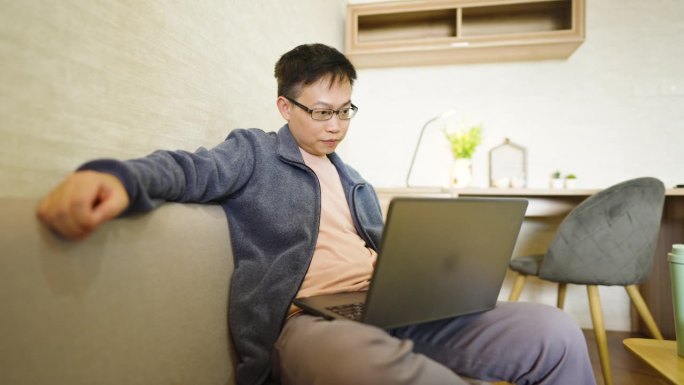 远程工作，男人在家里用笔记本电脑在客厅的沙发上工作