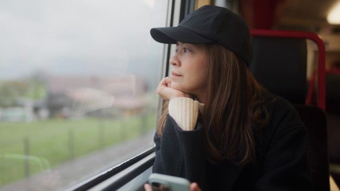 美丽的女游客坐在火车的窗边，透过窗户看风景