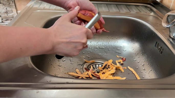 一个女孩在金属水槽上用蔬菜削皮器切红薯的皮，煮红薯